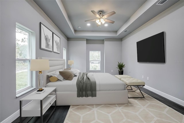 bedroom featuring multiple windows, wood-type flooring, a raised ceiling, and ceiling fan