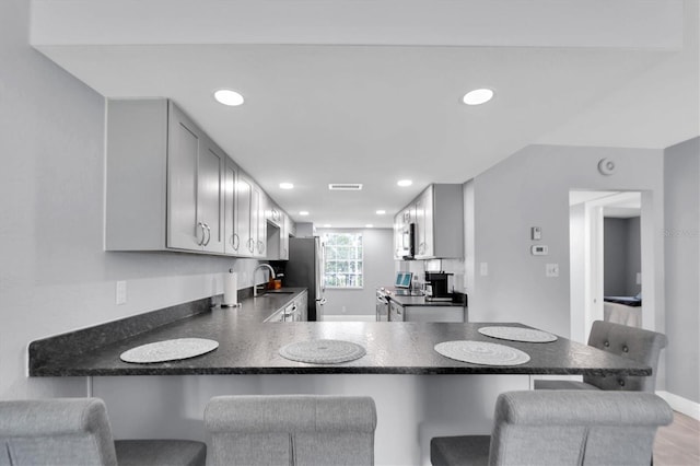 kitchen with a kitchen breakfast bar, kitchen peninsula, stainless steel refrigerator, and gray cabinetry