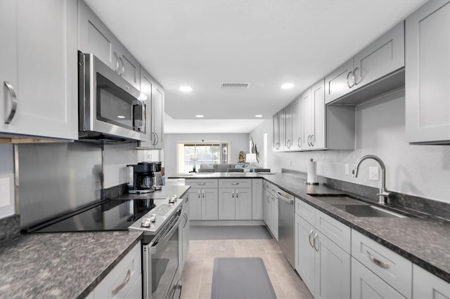 kitchen with light tile patterned floors, stainless steel appliances, dark stone counters, and sink