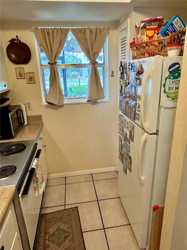 kitchen with white cabinets, range with electric cooktop, light tile patterned floors, and white refrigerator