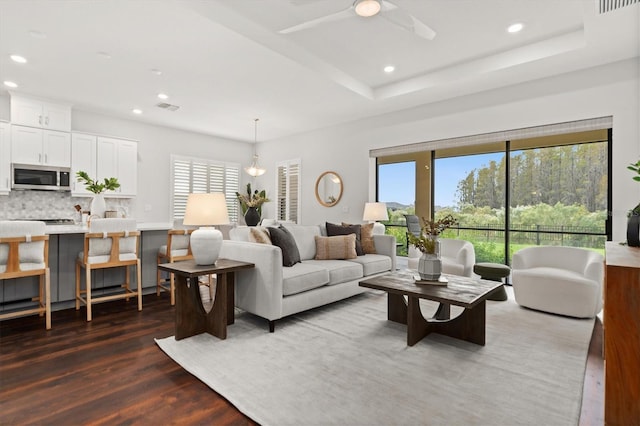 living room featuring dark wood-type flooring, ceiling fan, and a raised ceiling