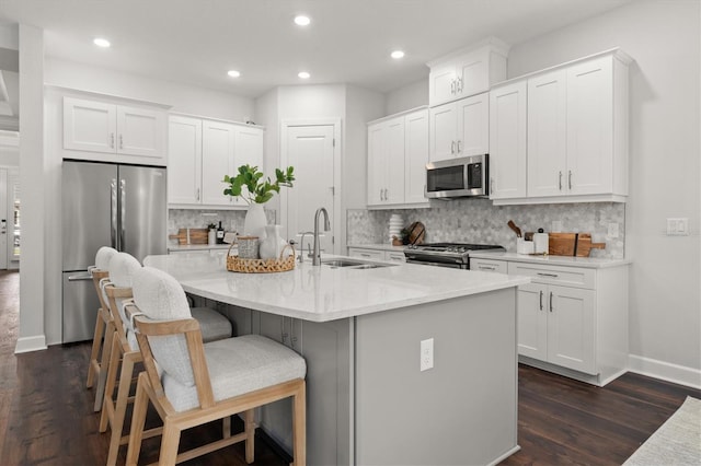 kitchen with stainless steel appliances, sink, an island with sink, white cabinets, and dark wood-type flooring