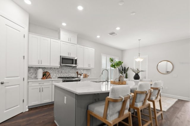 kitchen with white cabinets, appliances with stainless steel finishes, hanging light fixtures, and a center island with sink