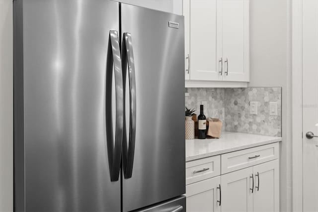 kitchen featuring white cabinets, backsplash, stainless steel refrigerator, and light stone countertops