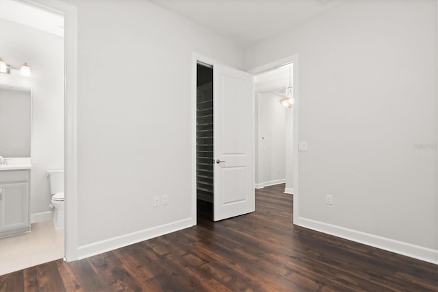 unfurnished bedroom with dark hardwood / wood-style flooring, a walk in closet, and ensuite bath