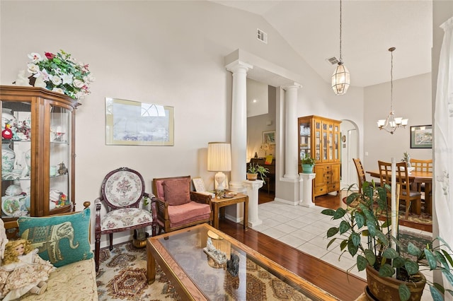 living room with a notable chandelier, light hardwood / wood-style floors, high vaulted ceiling, and decorative columns