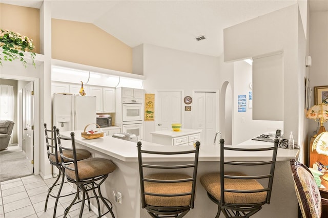 kitchen with a breakfast bar, lofted ceiling, white appliances, white cabinets, and light tile patterned floors