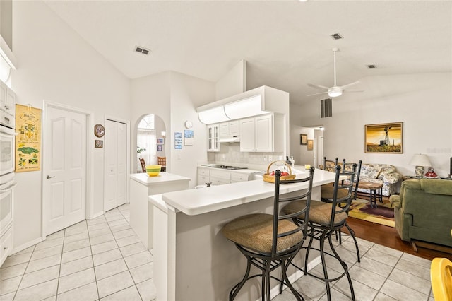 kitchen featuring white cabinets, a kitchen breakfast bar, ceiling fan, light tile patterned flooring, and kitchen peninsula