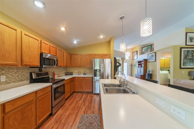 kitchen with light wood-type flooring, appliances with stainless steel finishes, hanging light fixtures, sink, and vaulted ceiling