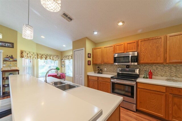 kitchen with vaulted ceiling, a center island with sink, sink, and appliances with stainless steel finishes