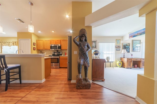 kitchen with light wood-type flooring, appliances with stainless steel finishes, decorative light fixtures, backsplash, and a breakfast bar area