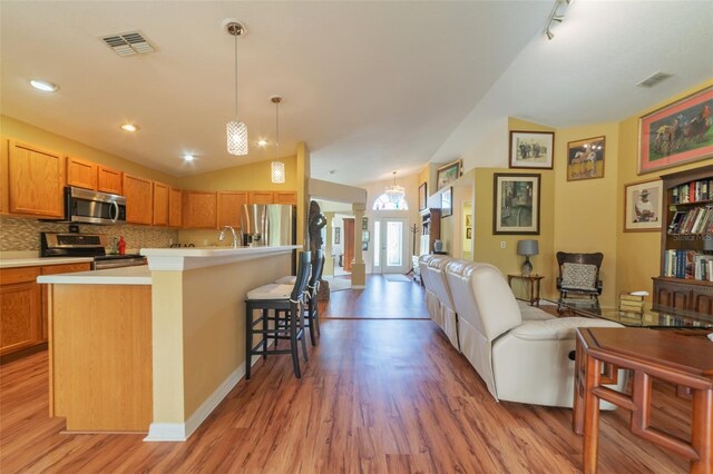 kitchen with appliances with stainless steel finishes, a kitchen bar, an island with sink, light hardwood / wood-style flooring, and lofted ceiling