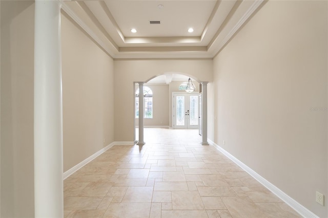 corridor featuring french doors, crown molding, a raised ceiling, and ornate columns