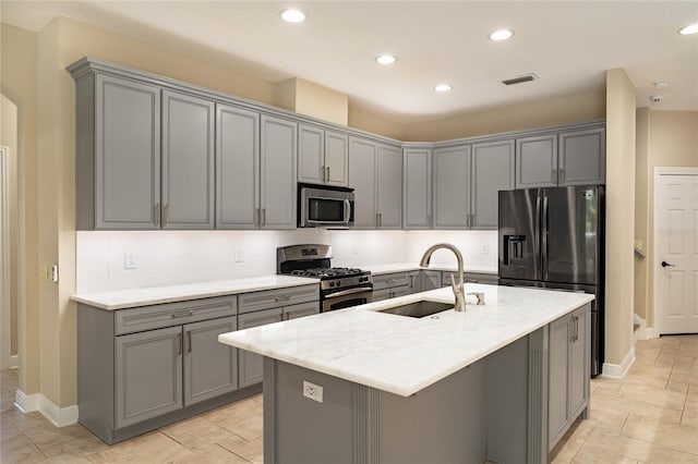 kitchen with stainless steel appliances, an island with sink, sink, and gray cabinetry