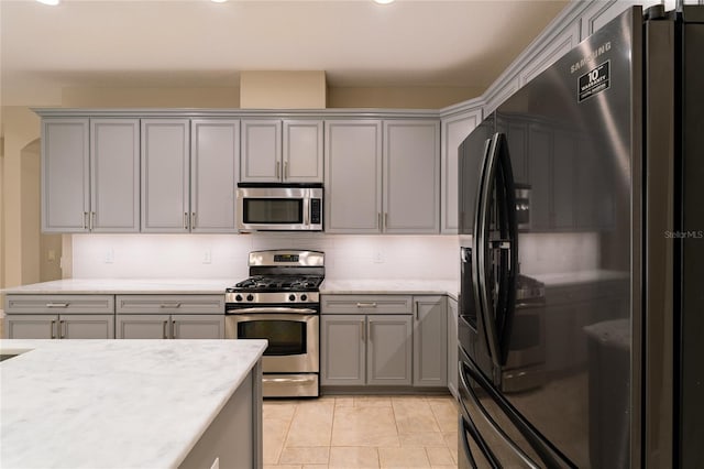 kitchen with light tile patterned floors, appliances with stainless steel finishes, gray cabinets, light stone countertops, and backsplash