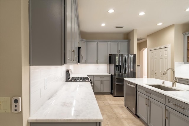 kitchen featuring sink, light stone counters, gray cabinets, stainless steel appliances, and backsplash