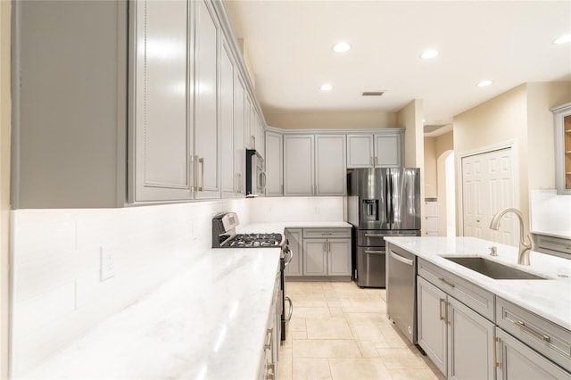 kitchen featuring sink, light tile patterned floors, gray cabinets, stainless steel appliances, and light stone countertops