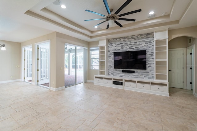 unfurnished living room with built in features, ceiling fan, and a tray ceiling