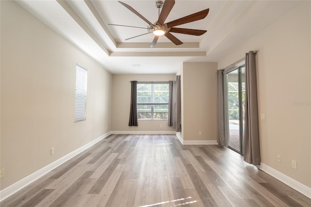 empty room with ceiling fan, wood-type flooring, and a raised ceiling