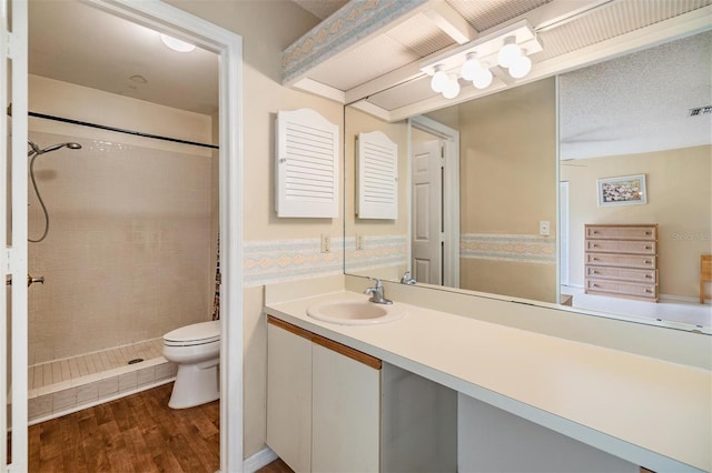 bathroom featuring wood-type flooring, vanity, toilet, and tiled shower