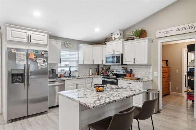 kitchen featuring stainless steel appliances, white cabinets, light wood-type flooring, and lofted ceiling