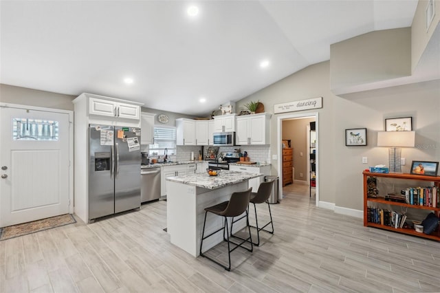 kitchen with stainless steel appliances, vaulted ceiling, white cabinets, a breakfast bar area, and a kitchen island