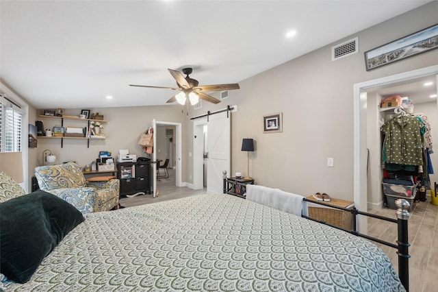 bedroom with a barn door, light hardwood / wood-style floors, ceiling fan, and vaulted ceiling