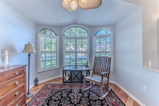 living area featuring ceiling fan, lofted ceiling, a textured ceiling, and light hardwood / wood-style floors