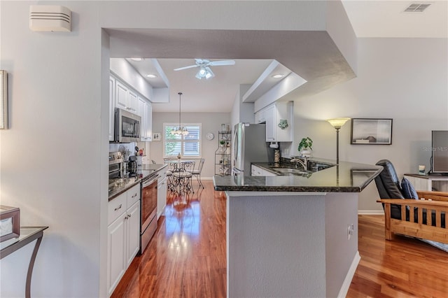 kitchen with white cabinets, kitchen peninsula, stainless steel appliances, and light wood-type flooring