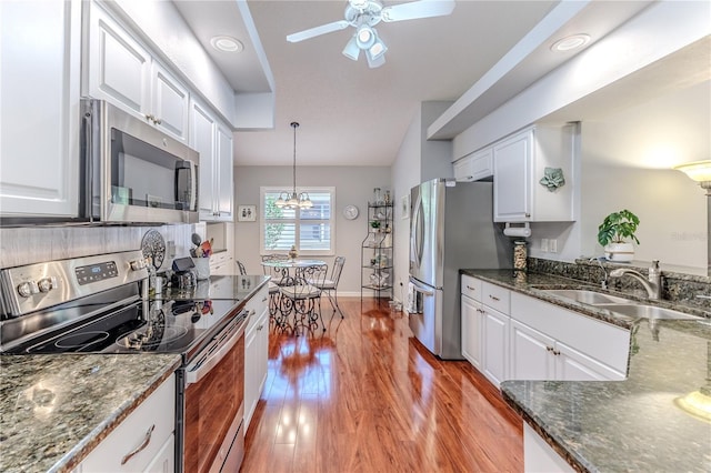 kitchen featuring stainless steel appliances, white cabinetry, sink, hanging light fixtures, and light wood-type flooring