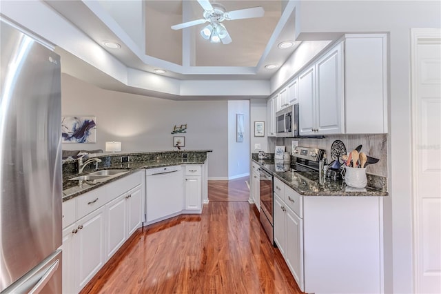 kitchen with dark stone counters, white cabinets, sink, light wood-type flooring, and appliances with stainless steel finishes