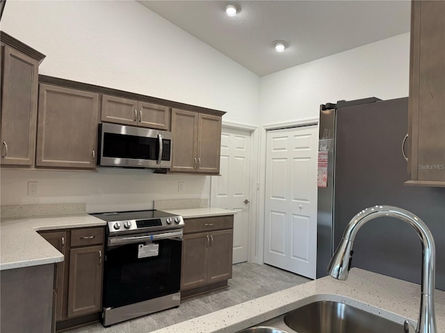 kitchen featuring light stone countertops, sink, stainless steel appliances, lofted ceiling, and light wood-type flooring