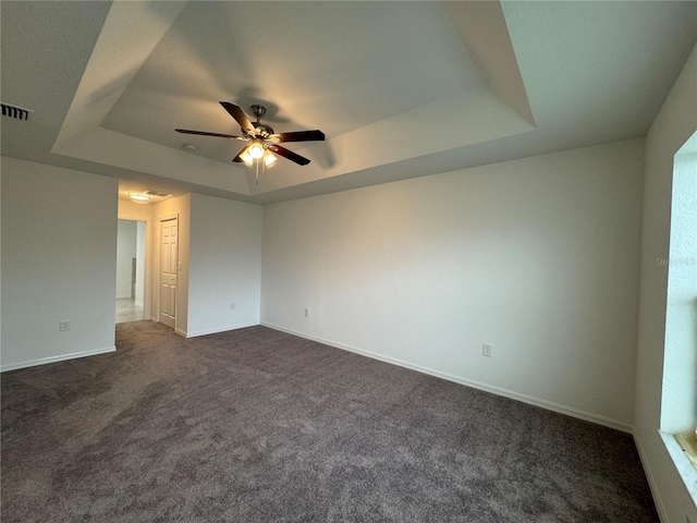 carpeted empty room featuring ceiling fan and a raised ceiling