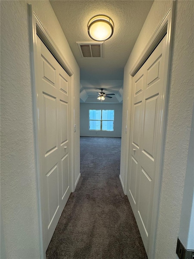 hallway featuring dark colored carpet and a textured ceiling