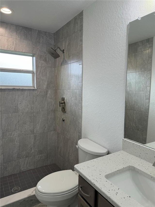 bathroom with tiled shower, vanity, and toilet