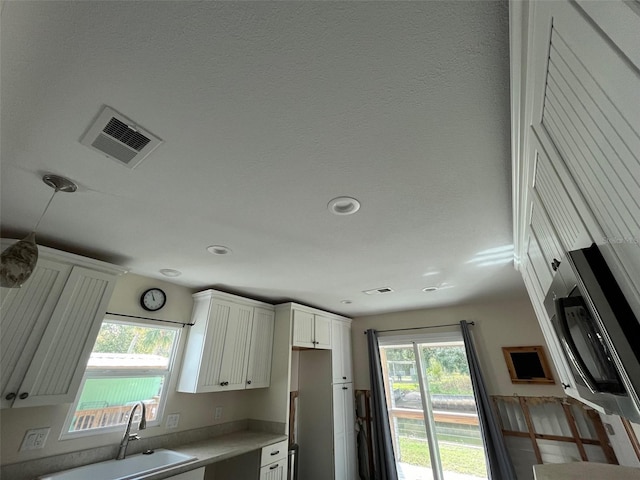 kitchen with a sink, plenty of natural light, light countertops, white cabinetry, and recessed lighting
