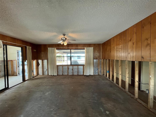 spare room featuring wooden walls, ceiling fan, and a textured ceiling