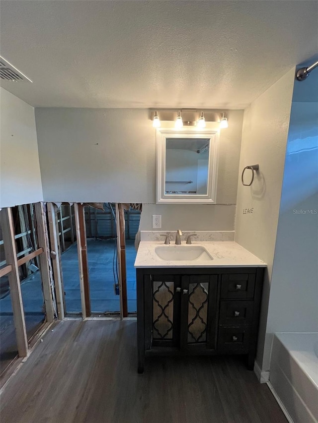 full bathroom with wood finished floors, vanity, a tub to relax in, and a textured ceiling