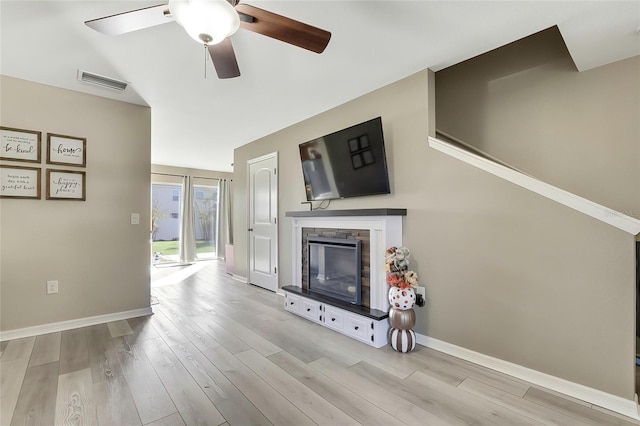 living room with light wood-type flooring, a stone fireplace, and ceiling fan