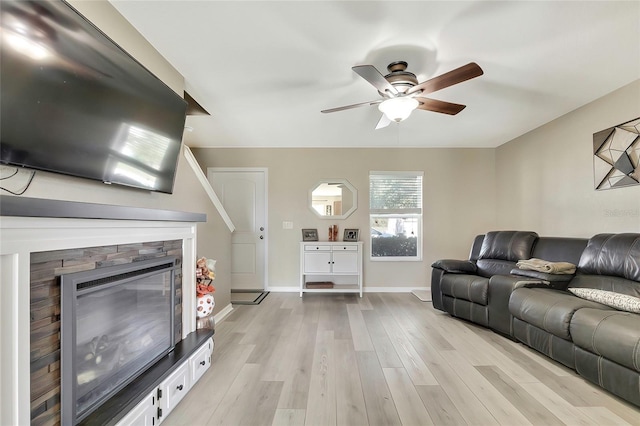 living room with ceiling fan, a stone fireplace, and light wood-type flooring