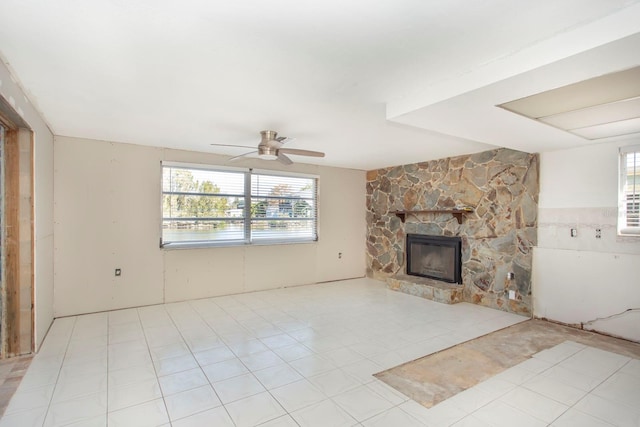 unfurnished living room featuring light tile patterned floors, a stone fireplace, and ceiling fan