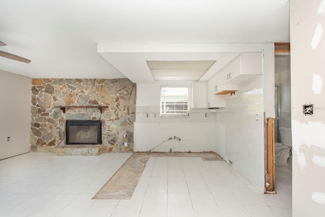 unfurnished living room with ceiling fan, a stone fireplace, and tile walls