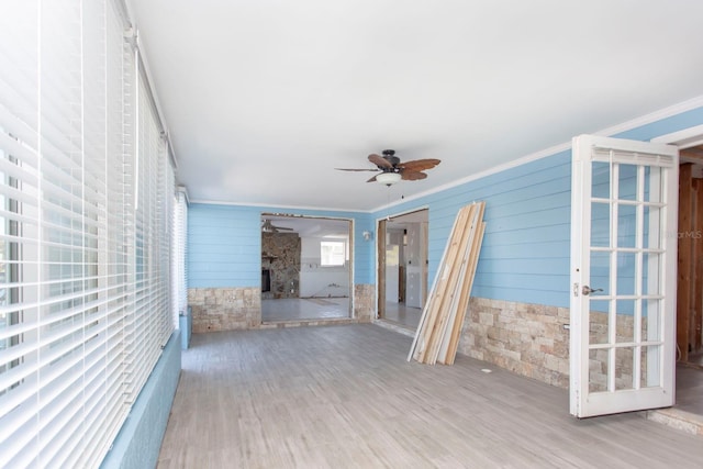 interior space with a stone fireplace, ceiling fan, hardwood / wood-style floors, and crown molding