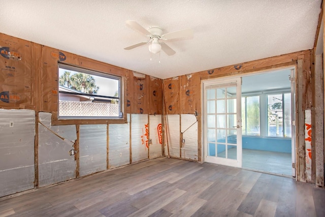 empty room with hardwood / wood-style floors, ceiling fan, wood walls, and a textured ceiling