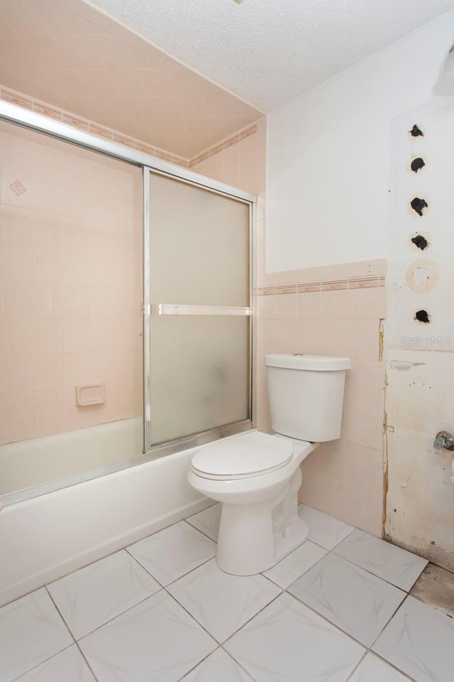 bathroom with a textured ceiling, toilet, tile walls, and enclosed tub / shower combo