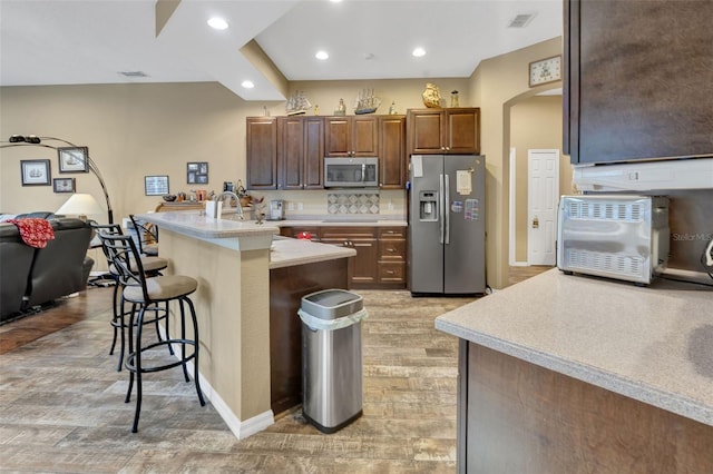 kitchen with stainless steel appliances, a kitchen breakfast bar, backsplash, an island with sink, and light wood-type flooring