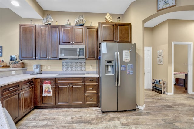 kitchen with appliances with stainless steel finishes, decorative backsplash, dark brown cabinetry, and light hardwood / wood-style floors