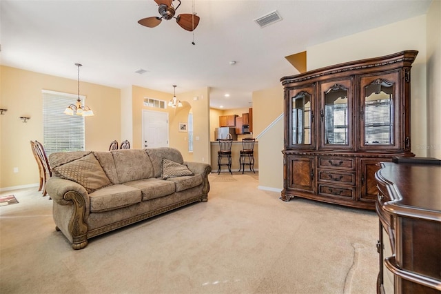 living room featuring ceiling fan with notable chandelier, light colored carpet, and a wealth of natural light