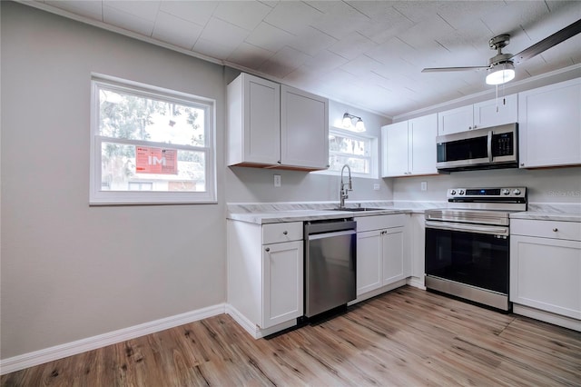 kitchen with stainless steel appliances, white cabinetry, sink, crown molding, and light wood-type flooring