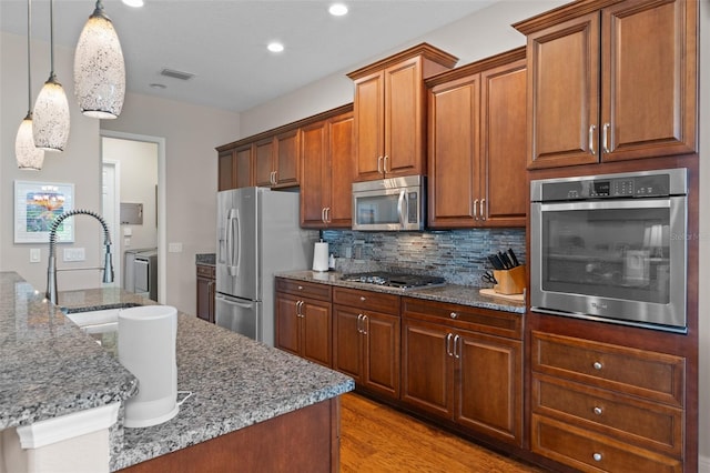 kitchen with decorative light fixtures, stainless steel appliances, light hardwood / wood-style flooring, and an island with sink